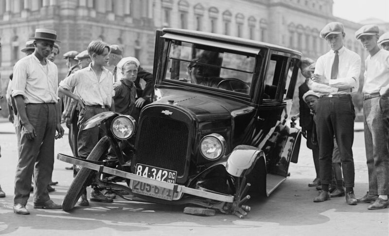 grayscale photo of people standing near the wrecked vintage car