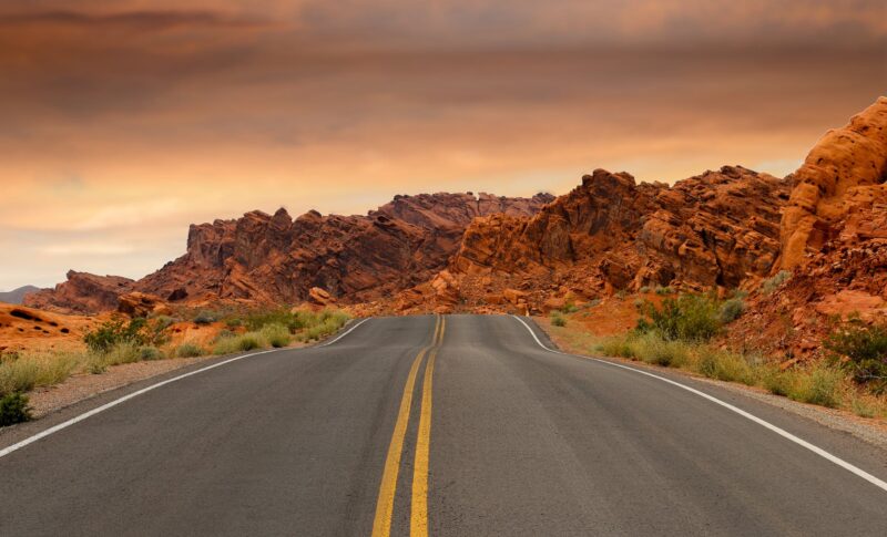 gray concrete road beside brown mountain during golden hour