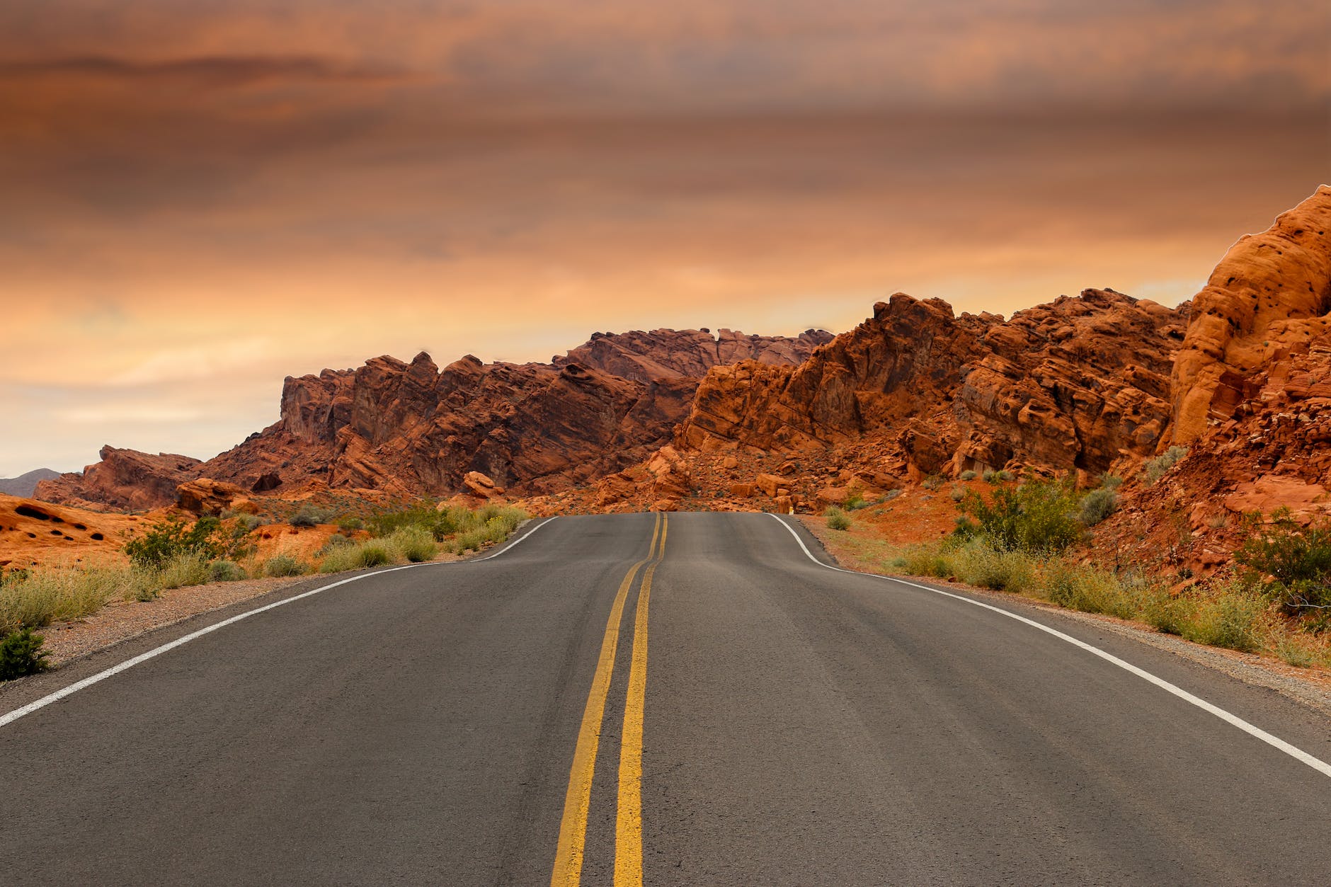 gray concrete road beside brown mountain during golden hour