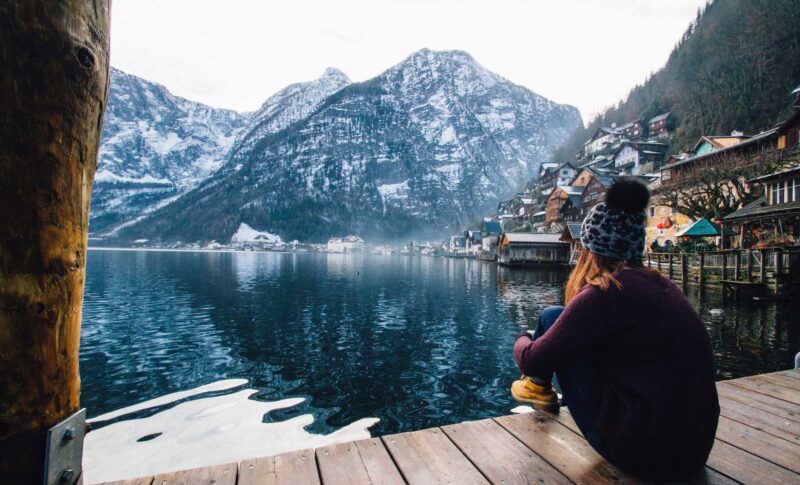 woman in purple sweater sitting on wooden floor with view of lake and mountains