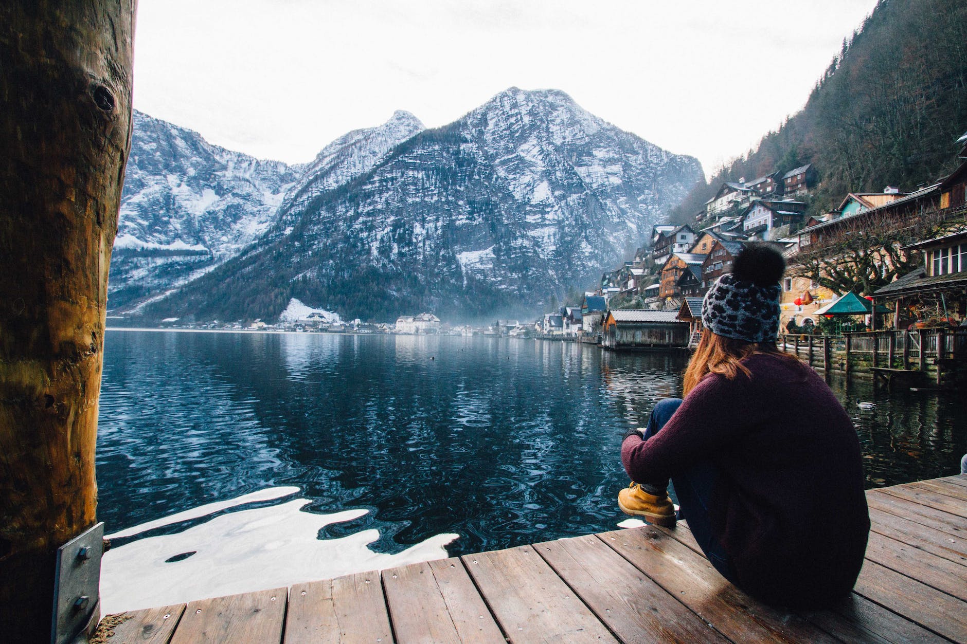 woman in purple sweater sitting on wooden floor with view of lake and mountains